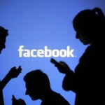 People pose with mobile devices in front of projection of Facebook logo in this picture illustration taken in Zenica
